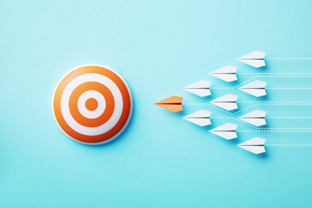 Paper planes flyıng towards an orange bull's eye target on blue background, Target concept.